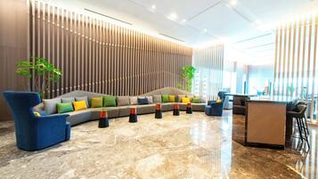 A modern lobby with a sectional sofa, a blue armchair, and a glass-top coffee table.
