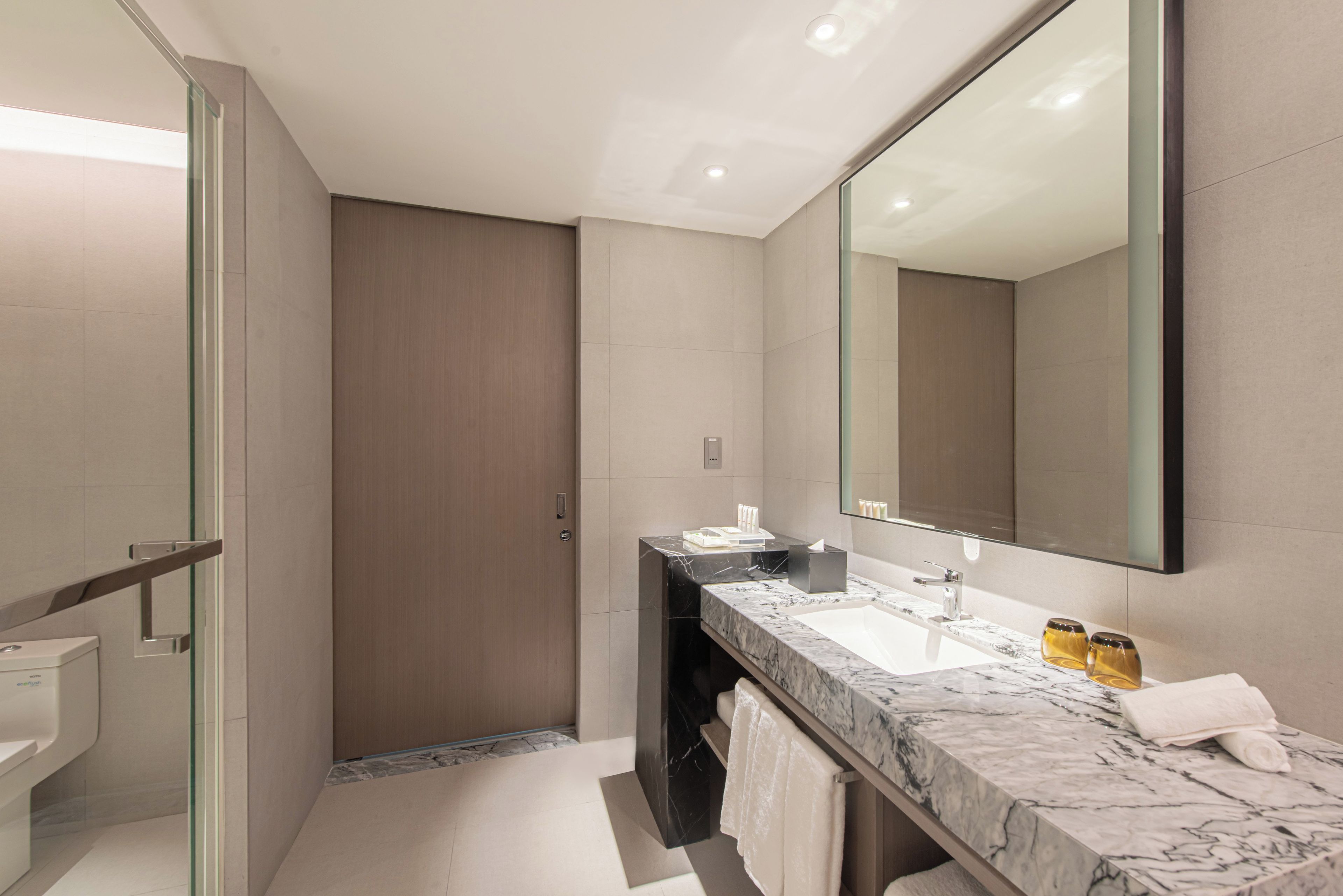 Un baño moderno con cabina de ducha de vidrio, lavabo de mármol y un espejo grande.