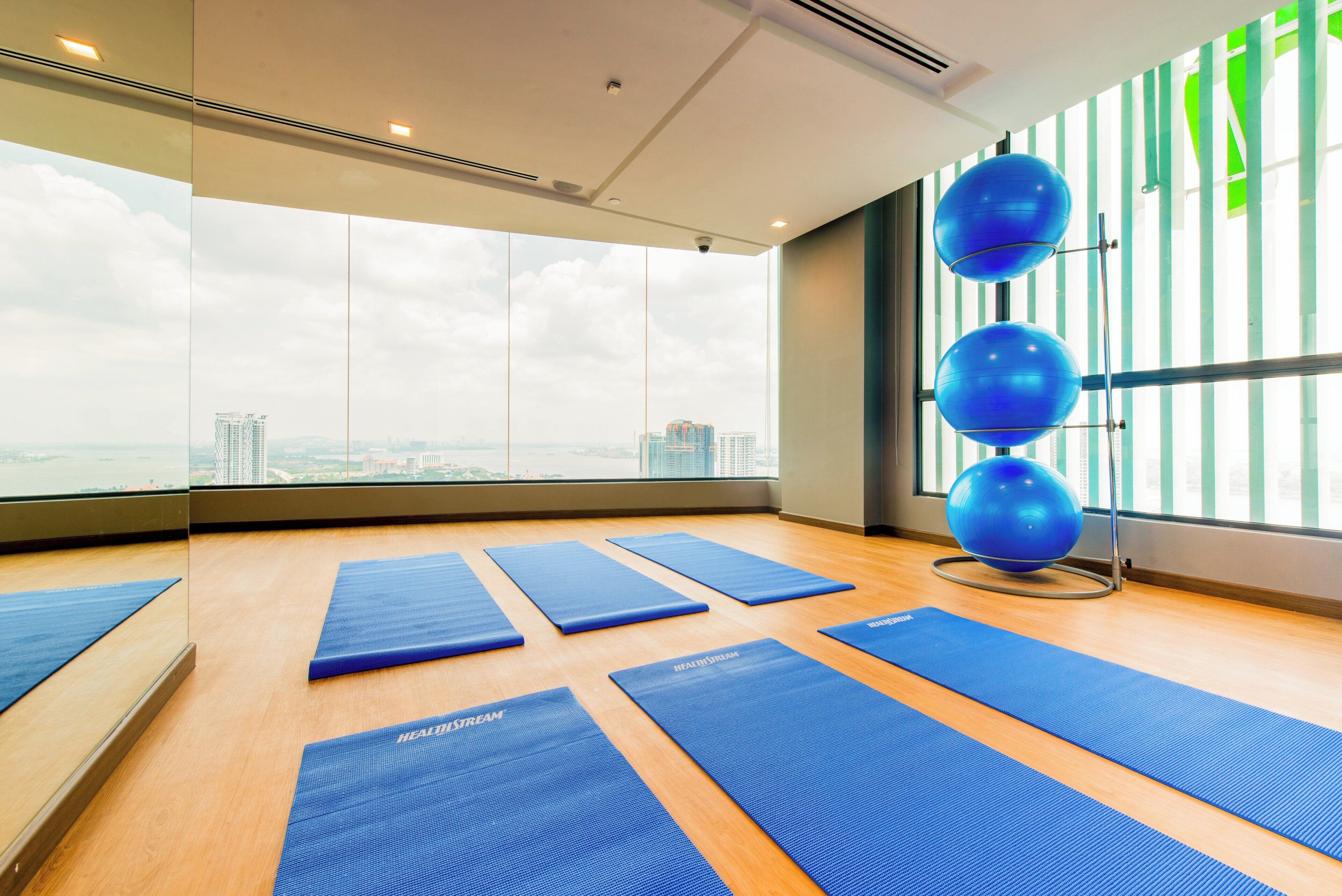 A spacious room with large windows, exercise mats, and a blue exercise ball.