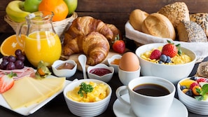 A breakfast setting with croissants, bread, cheese, fruits, and beverages.