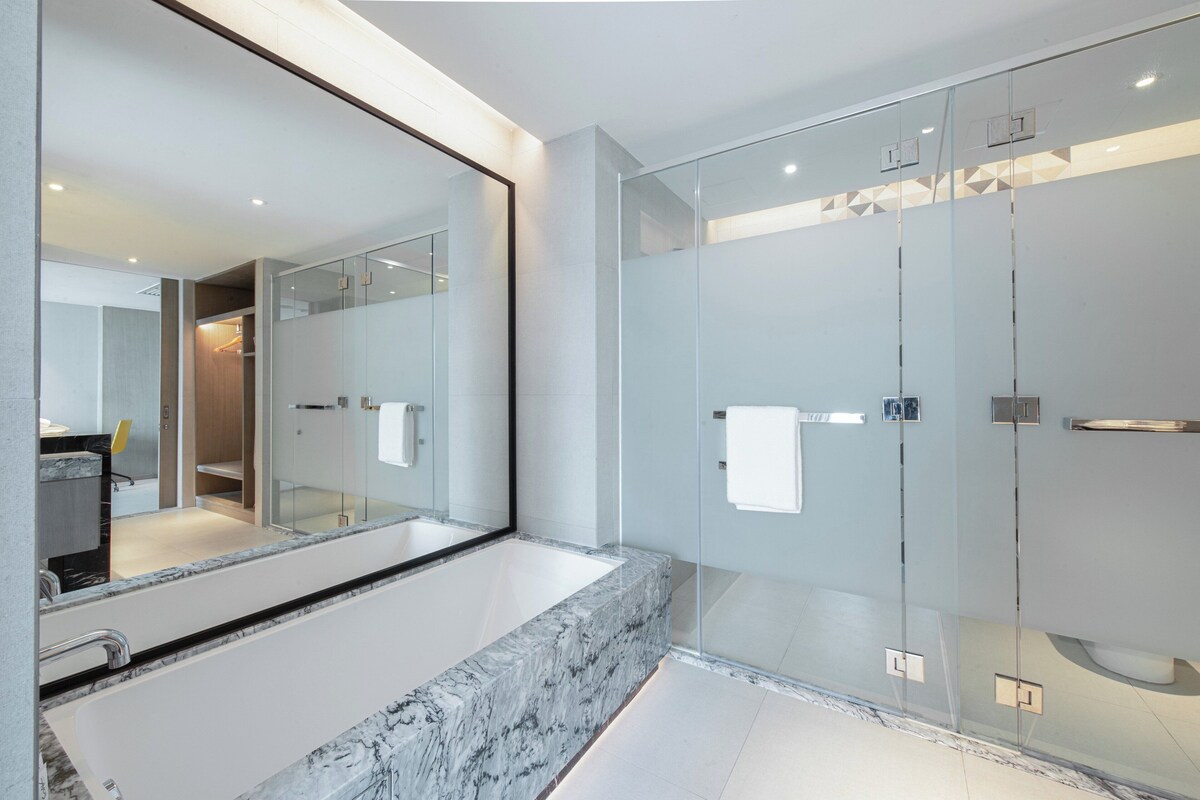 A modern bathroom with a large mirror, a glass shower enclosure, and a marble countertop.