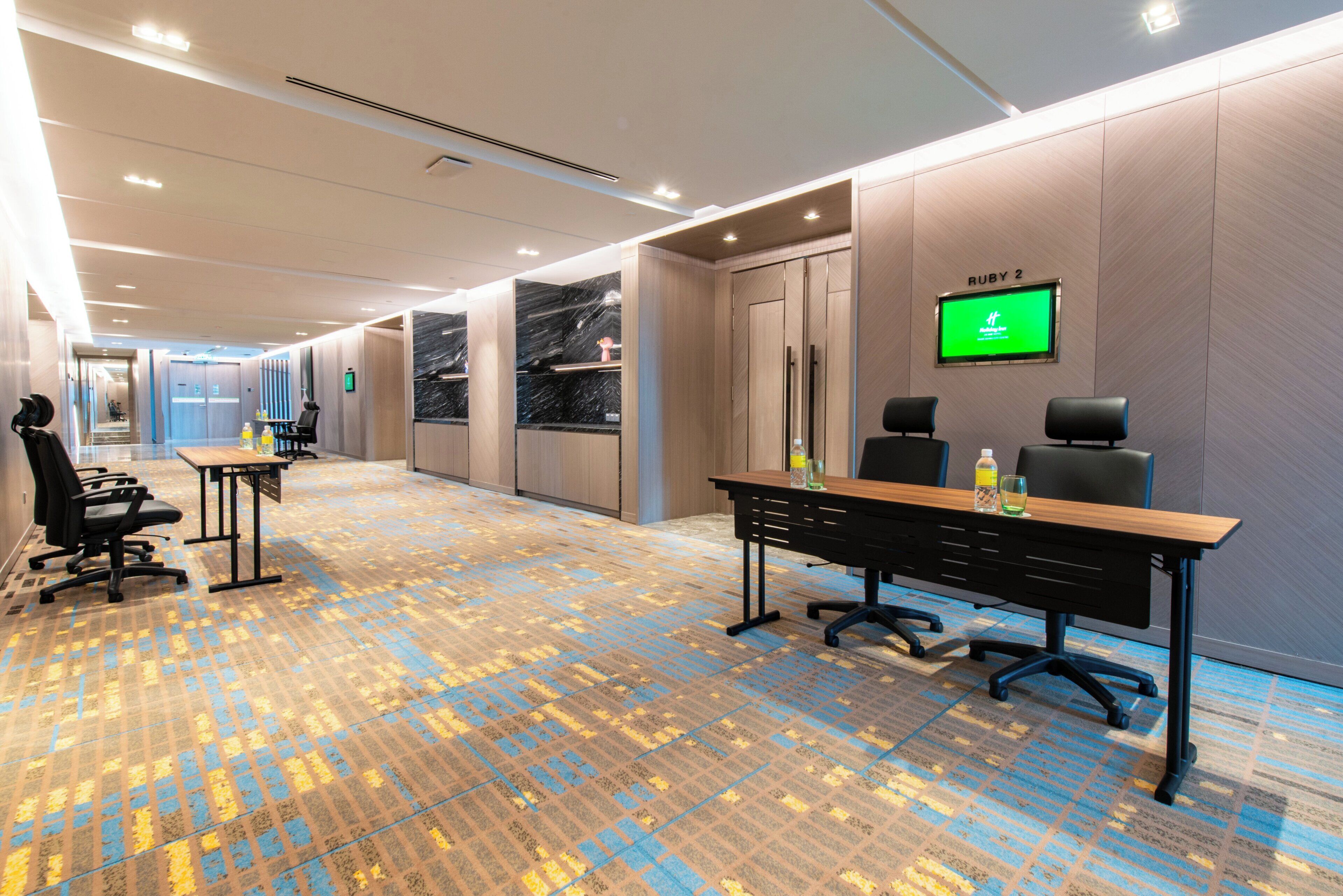 A modern conference room with a long table, chairs, and a large screen displaying a green screen.
