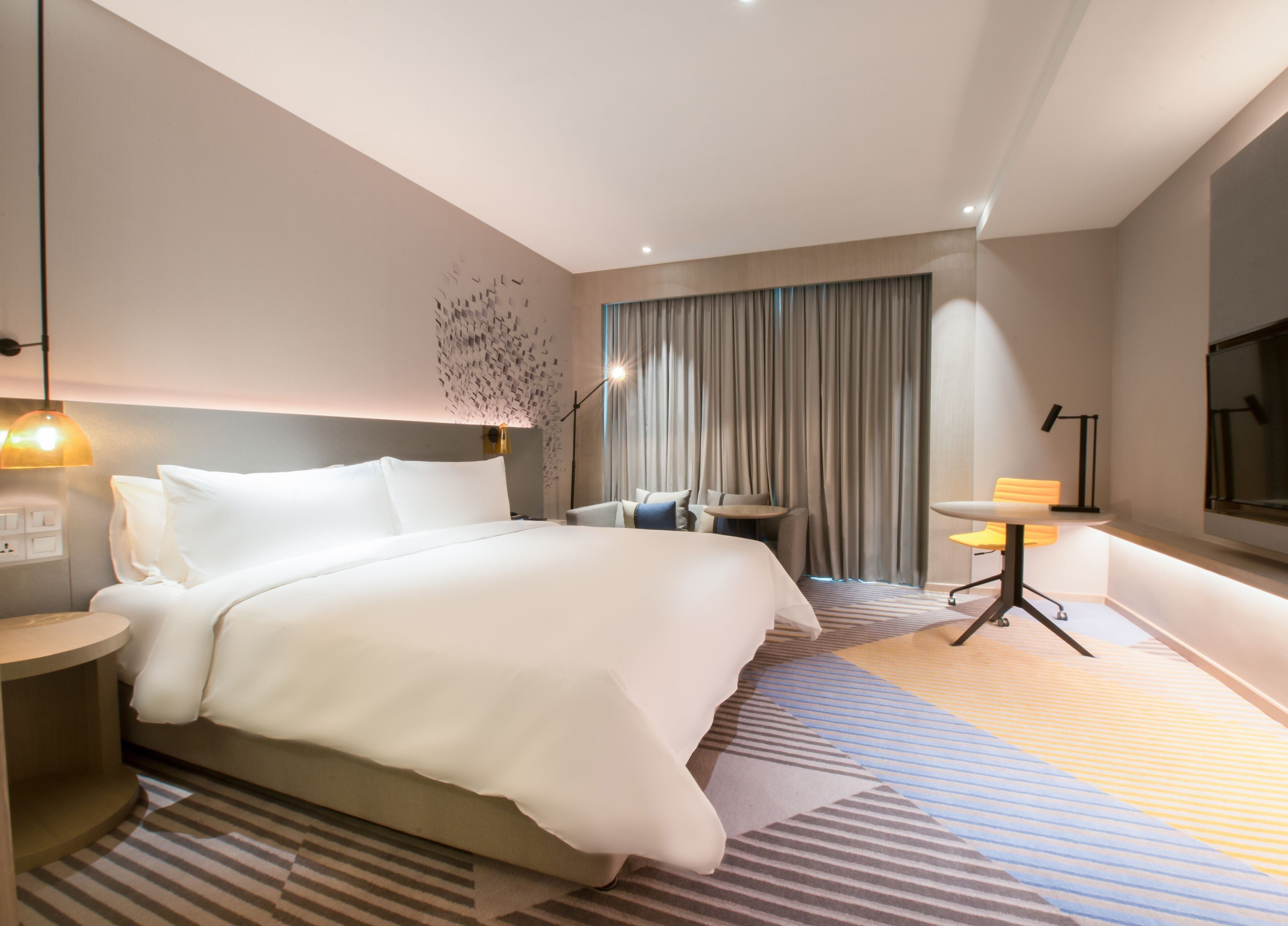 Una habitación de hotel moderna con una cama grande, un escritorio, una silla y un televisor.