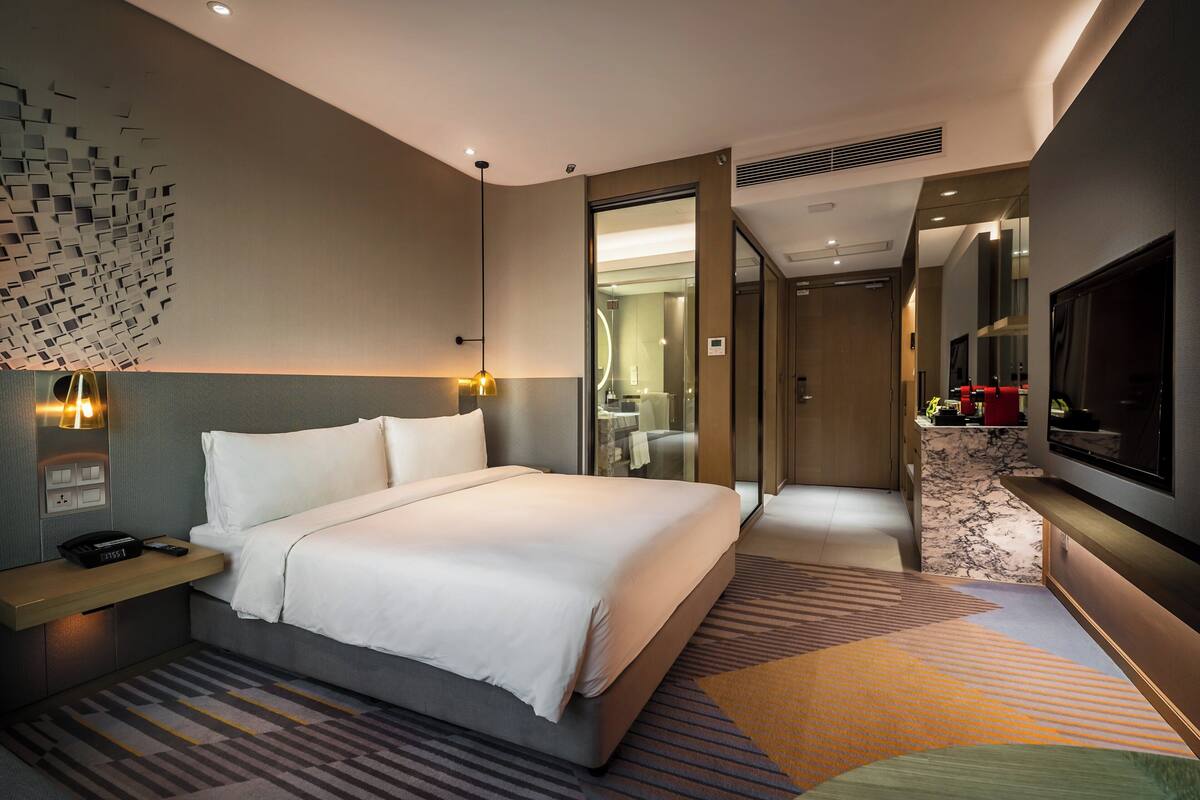 A modern hotel room with a large bed, bedside table, and a TV.