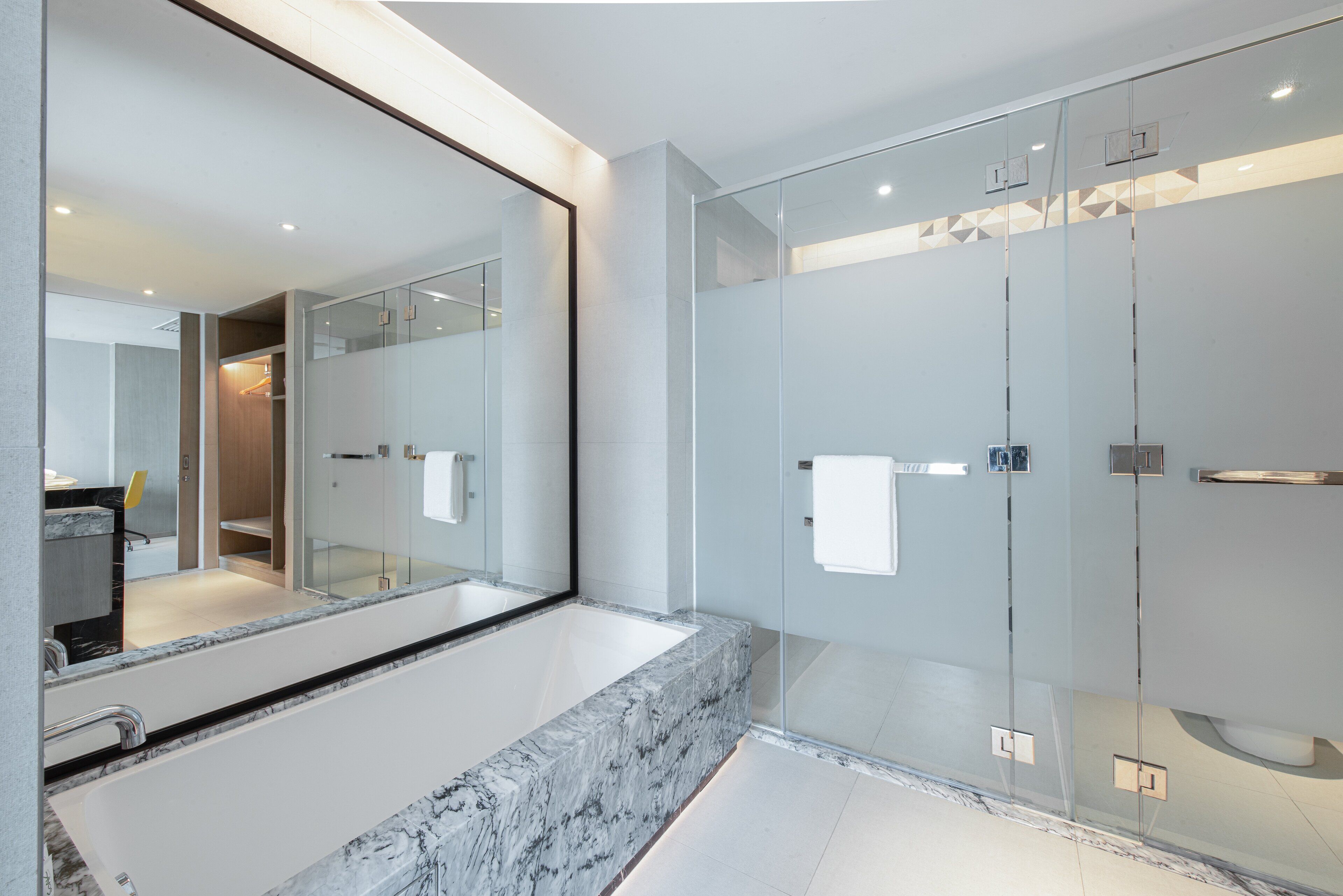 A modern bathroom with a large mirror, a marble sink, and a glass shower enclosure.