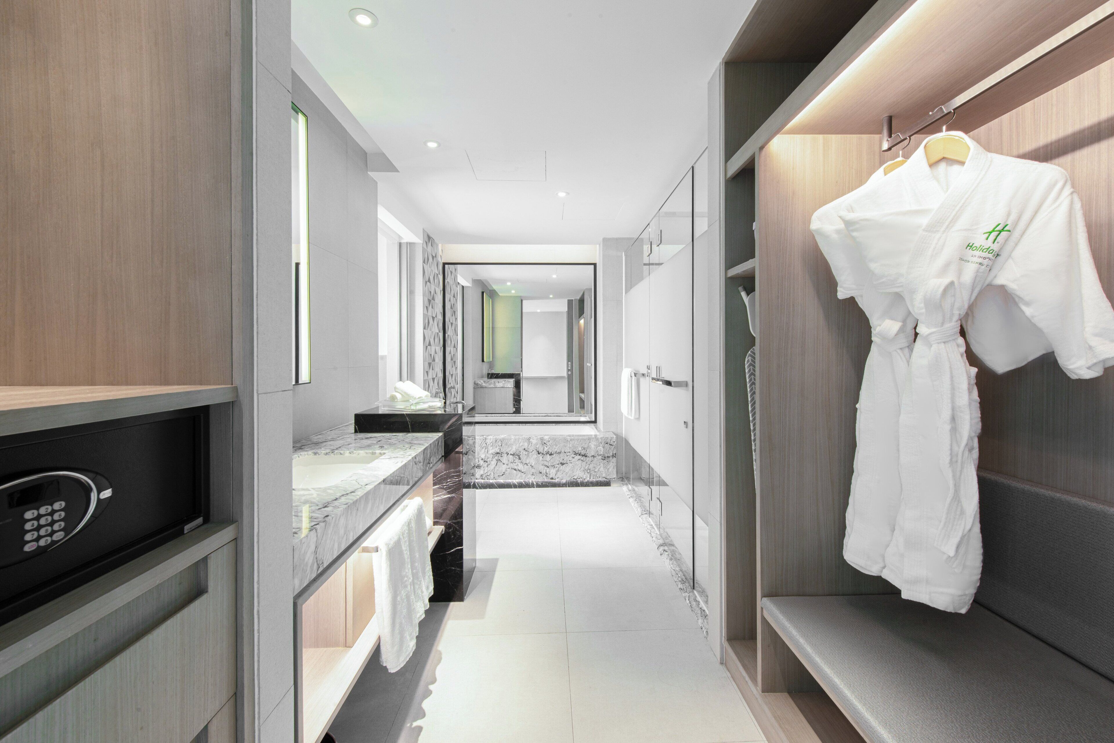 A modern hotel bathroom with a marble vanity, a walk-in shower, and a robe hanging on a rack.