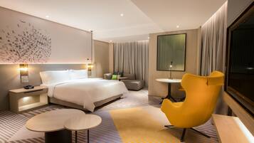 Une chambre d’hôtel moderne avec un grand lit, un canapé, un fauteuil jaune, une petite table et une grande fenêtre.