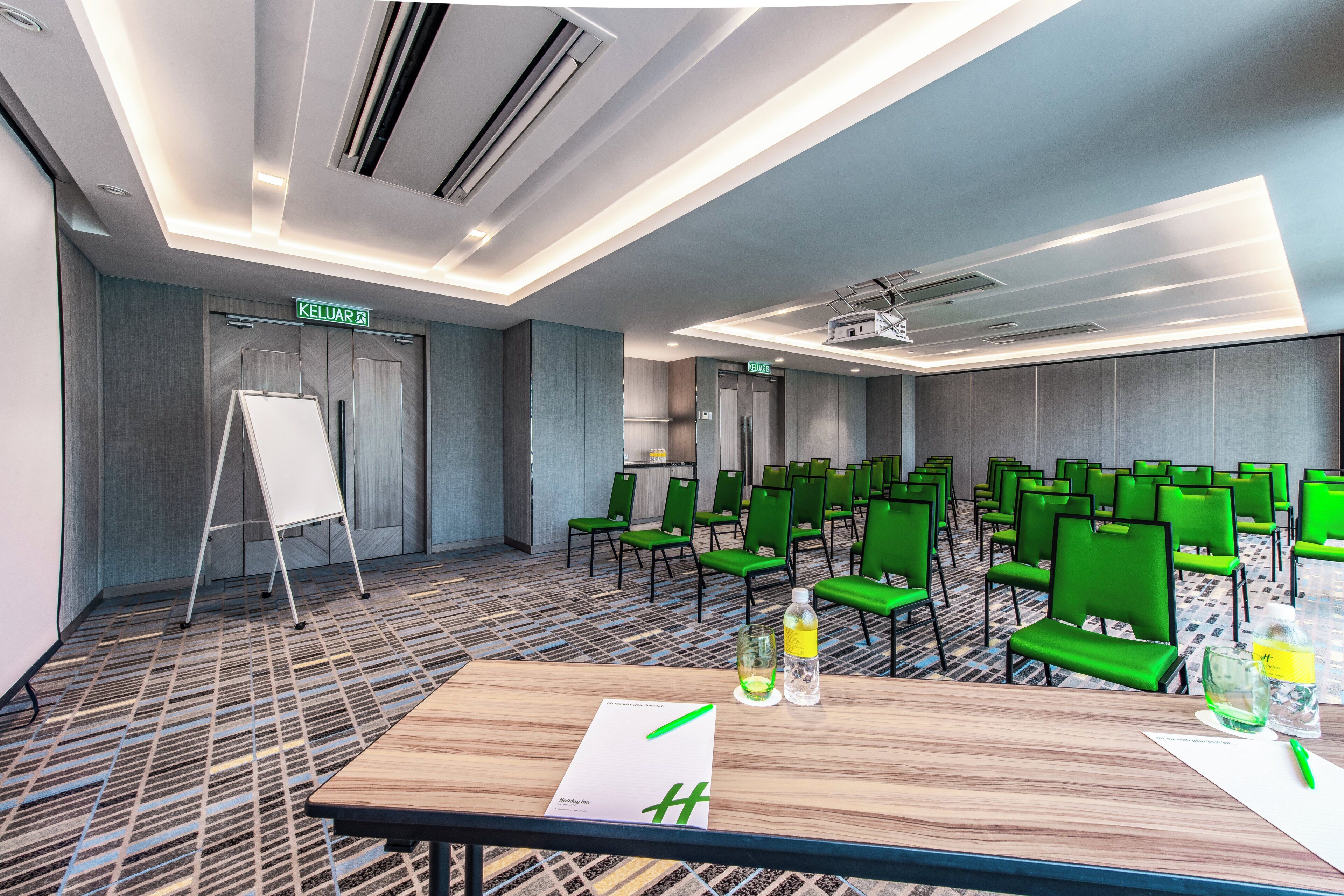 A conference room with a large table, green chairs, a whiteboard, and a projector screen.