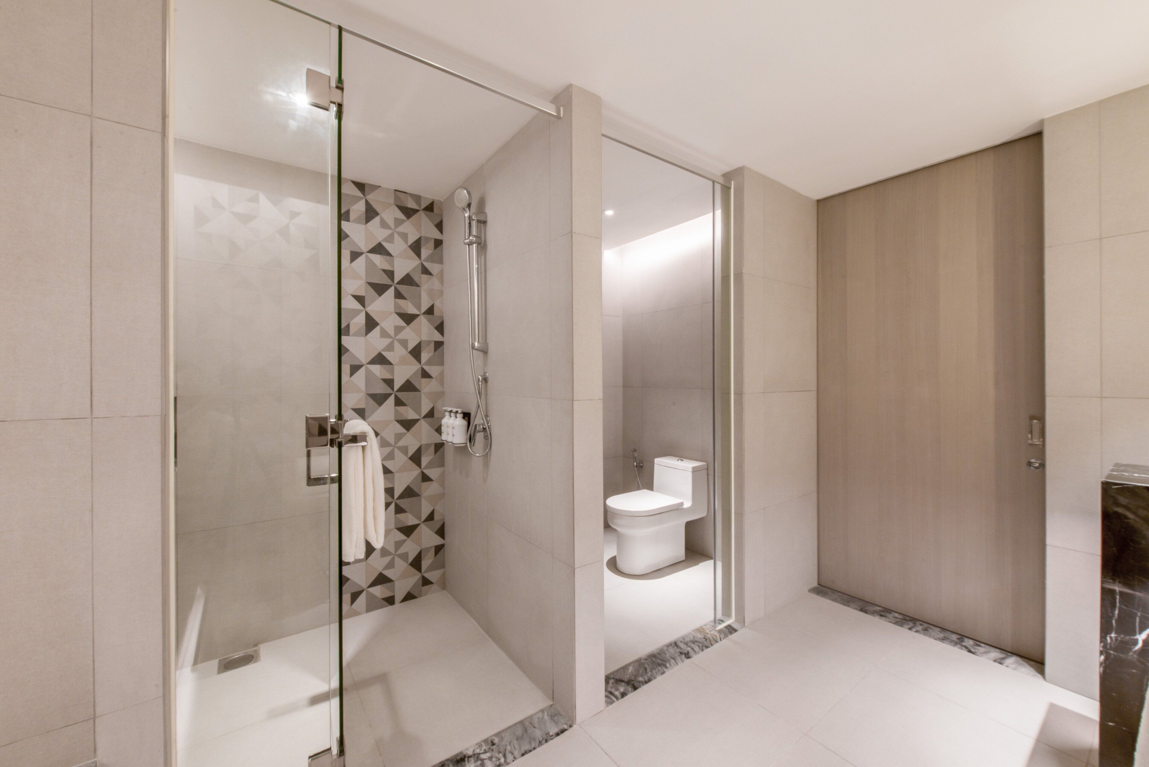 Een moderne badkamer met een glazen douchecabine, een toilet en een vloer van marmer.