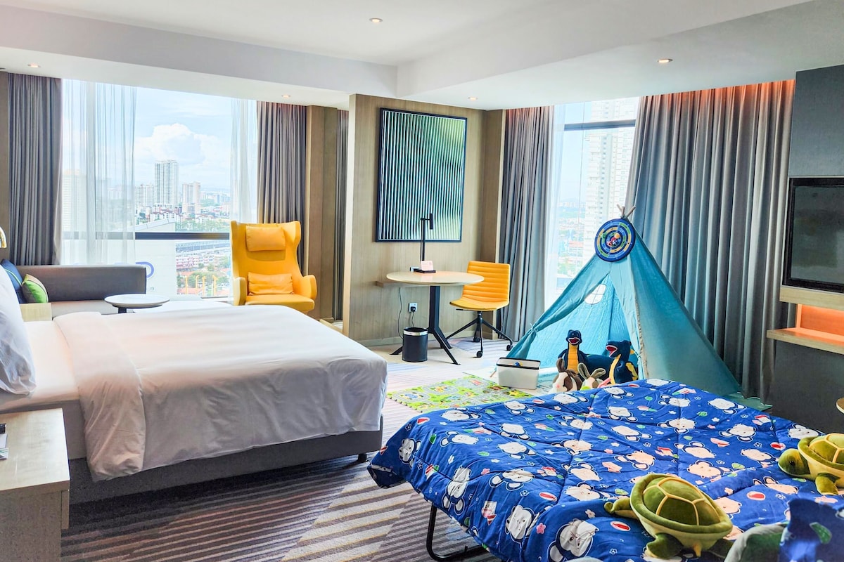 A hotel room with a bed, a desk, a chair, a TV, and a window with a city view.