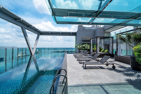 A rooftop infinity pool with lounge chairs and a glass ceiling overlooking the ocean.