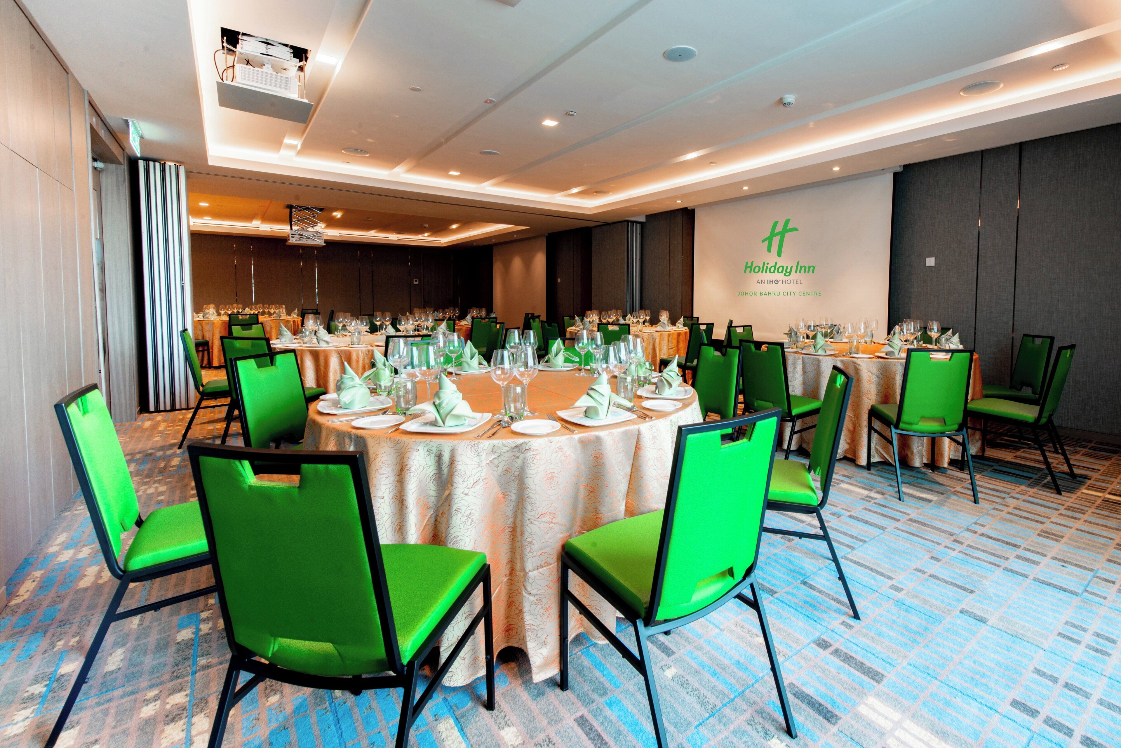 A conference room with round tables, green chairs, and a large screen.