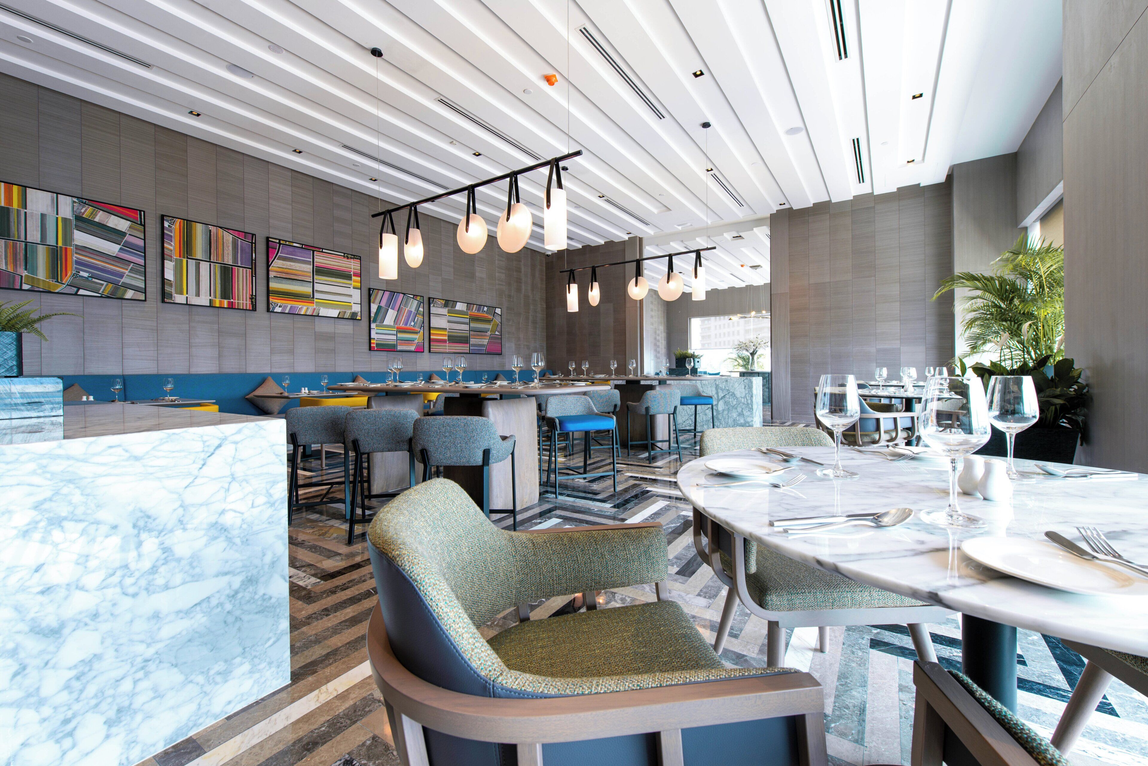 A modern restaurant interior with a bar area, seating, and a view of the city.