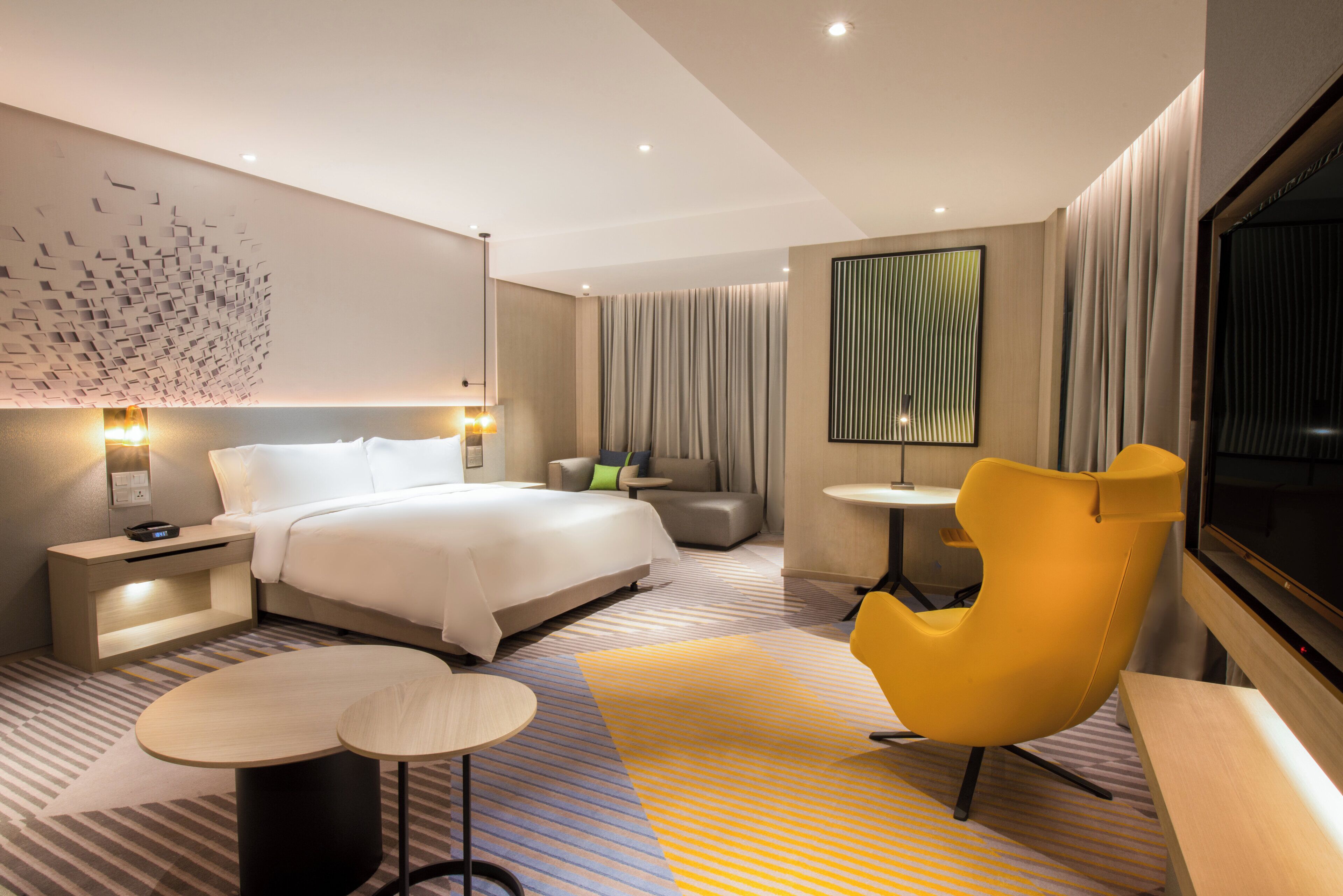 A modern hotel room with a large bed, bedside tables, a desk, a chair, and a TV.