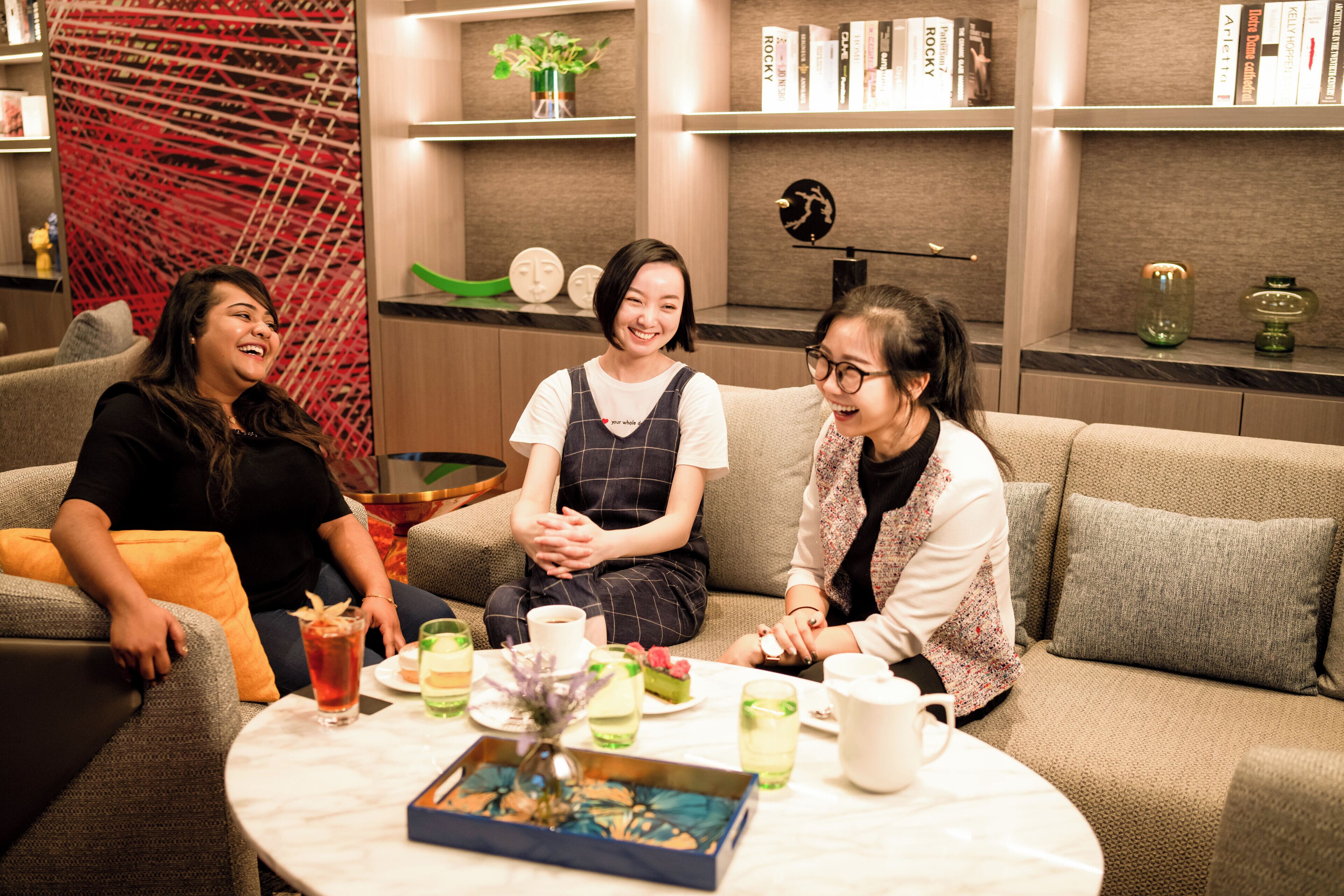 Three people sitting on a sofa in a modern lounge area with a round table in front of them, featuring drinks and a small decorative item.