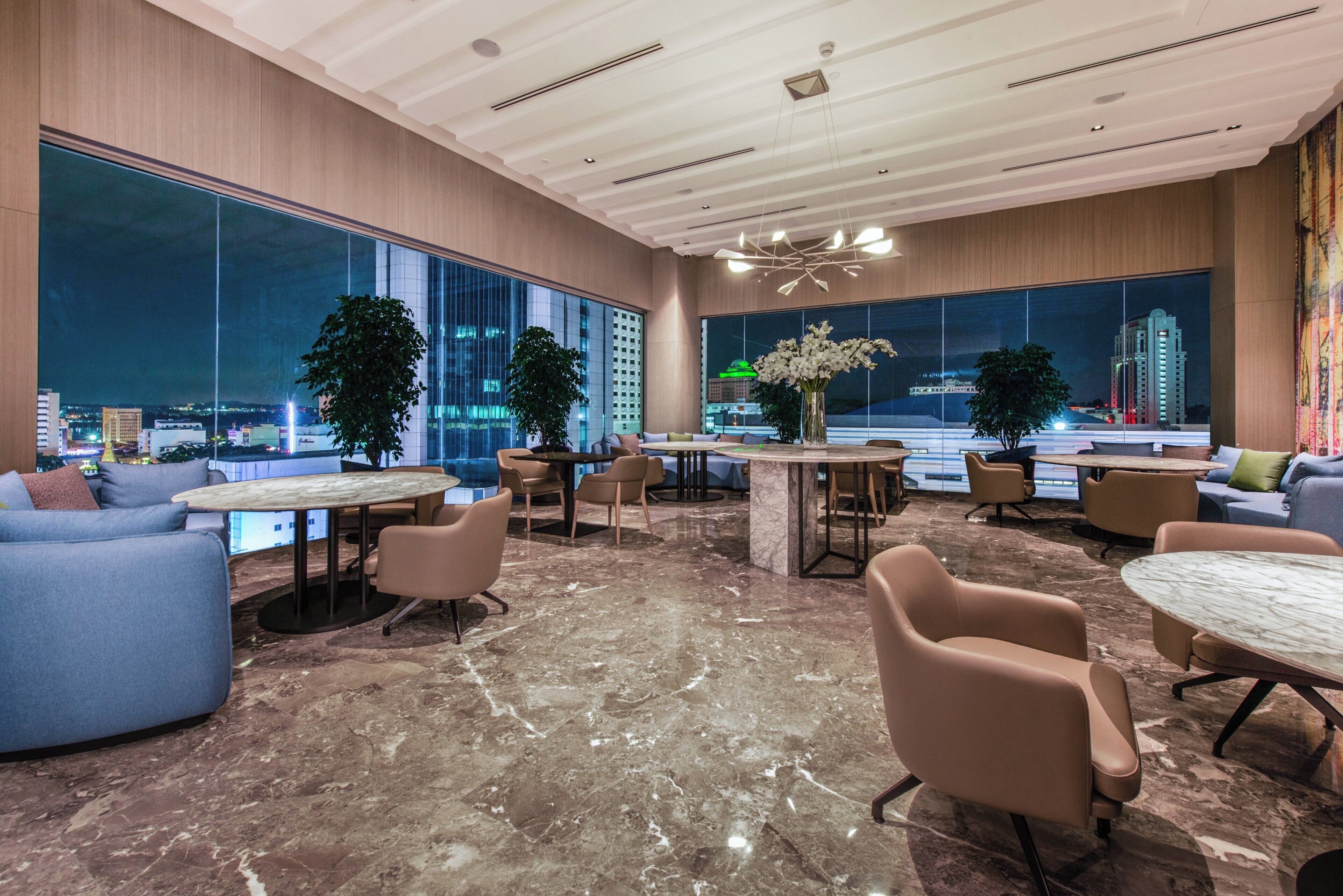 A modern hotel lobby with a marble floor, large windows offering city views, and contemporary furniture.