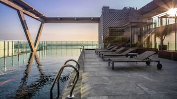 Un espace piscine aménagé sur le toit, avec des chaises longues et une rambarde en verre donnant sur une étendue d’eau.