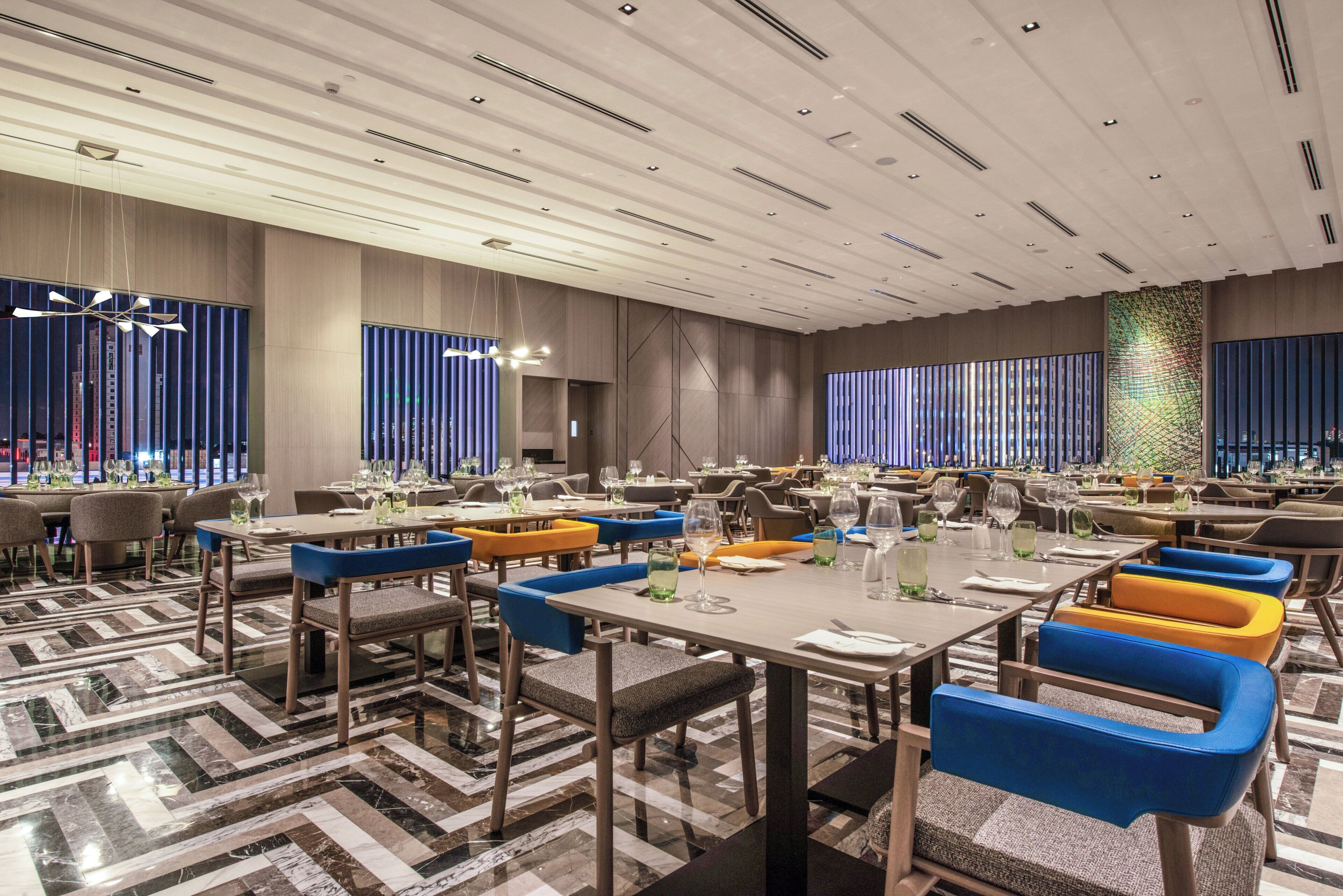 A modern dining area with multiple tables and chairs, a patterned floor, and a ceiling with recessed lighting.