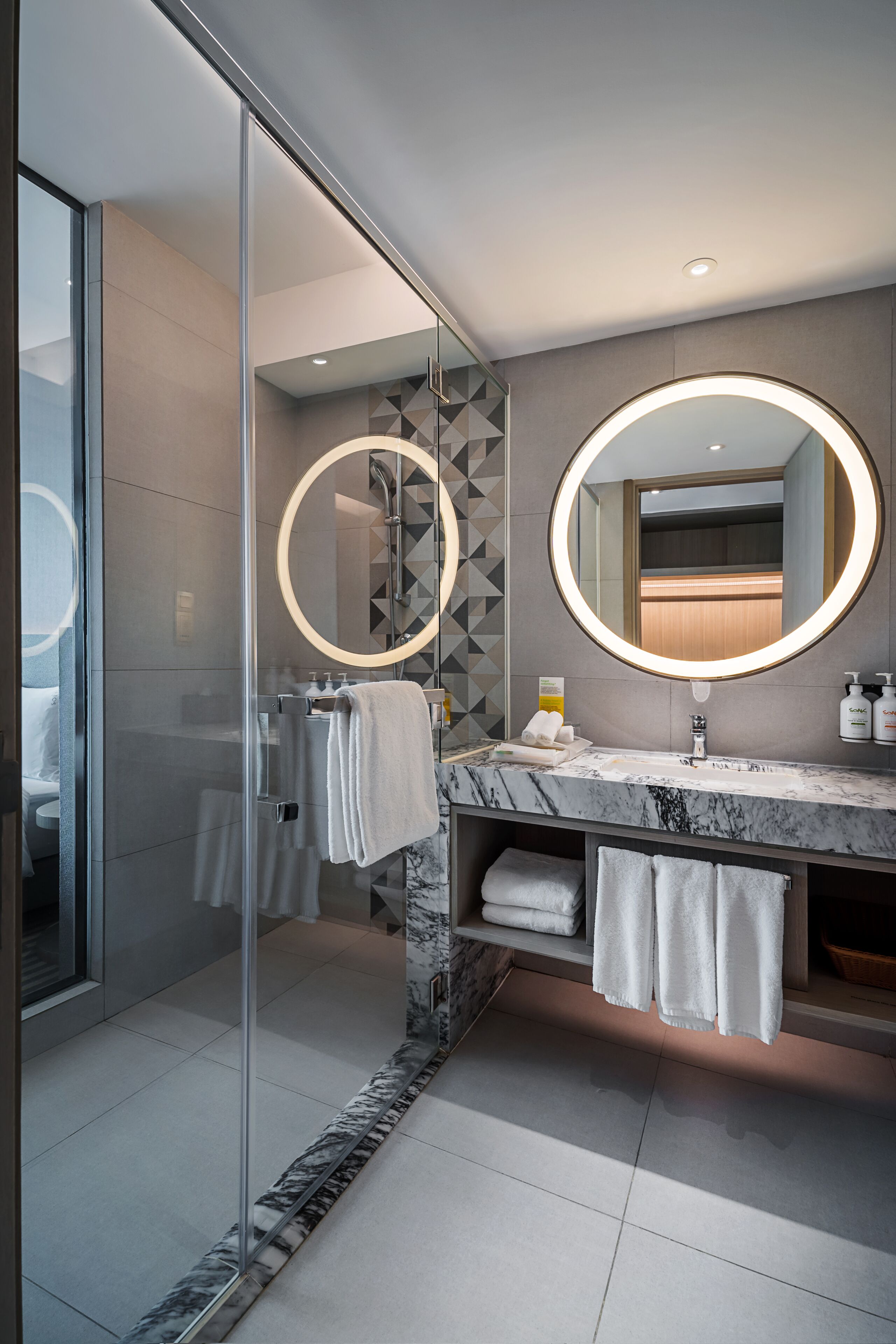 A modern bathroom with a glass shower enclosure, marble vanity, and dual round mirrors.