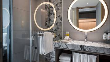 Un baño moderno con cabina de ducha de vidrio, tocador de mármol y dos espejos redondos.
