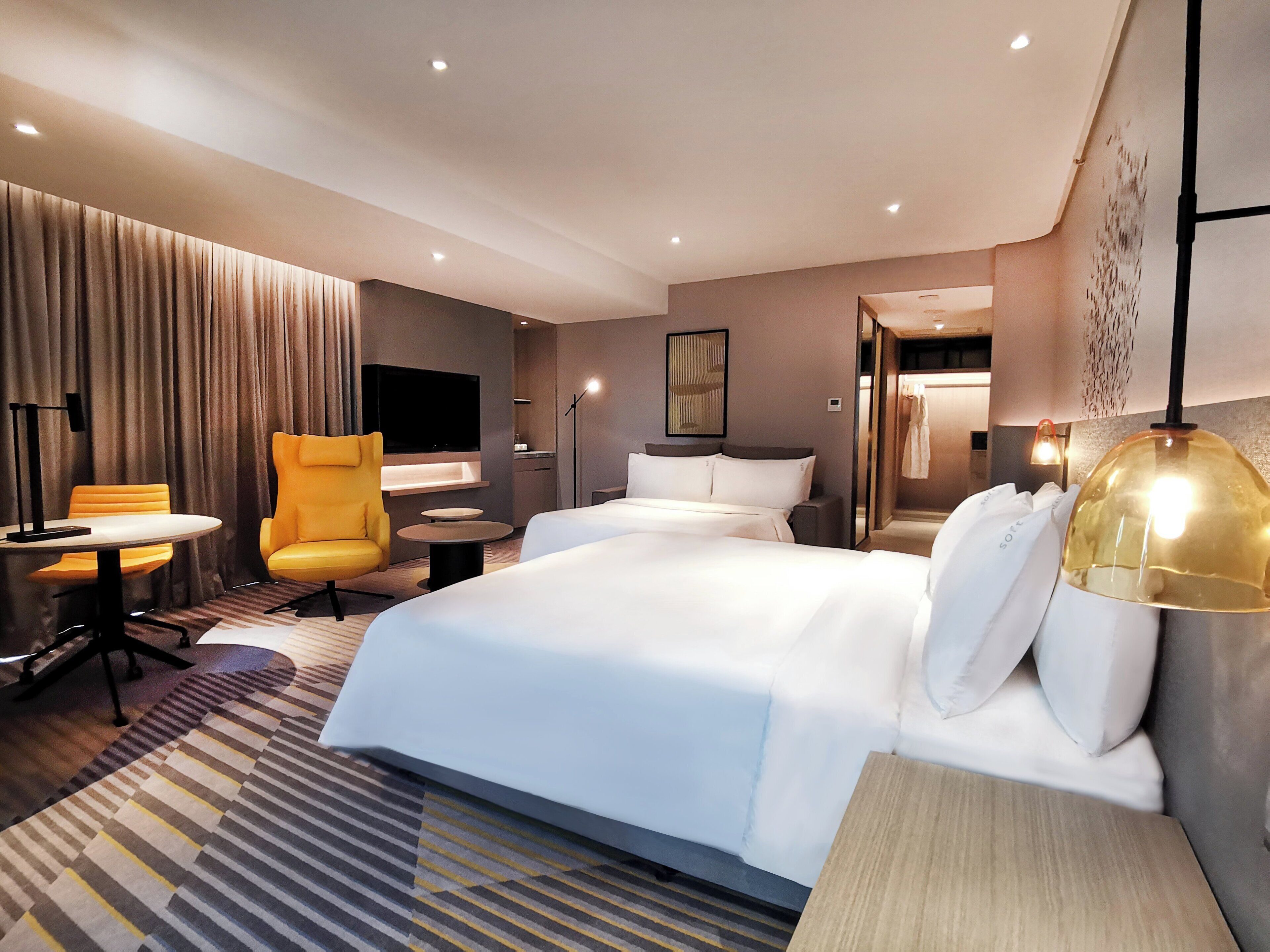 A hotel room with a large bed, a desk, a chair, a TV, and a lamp.