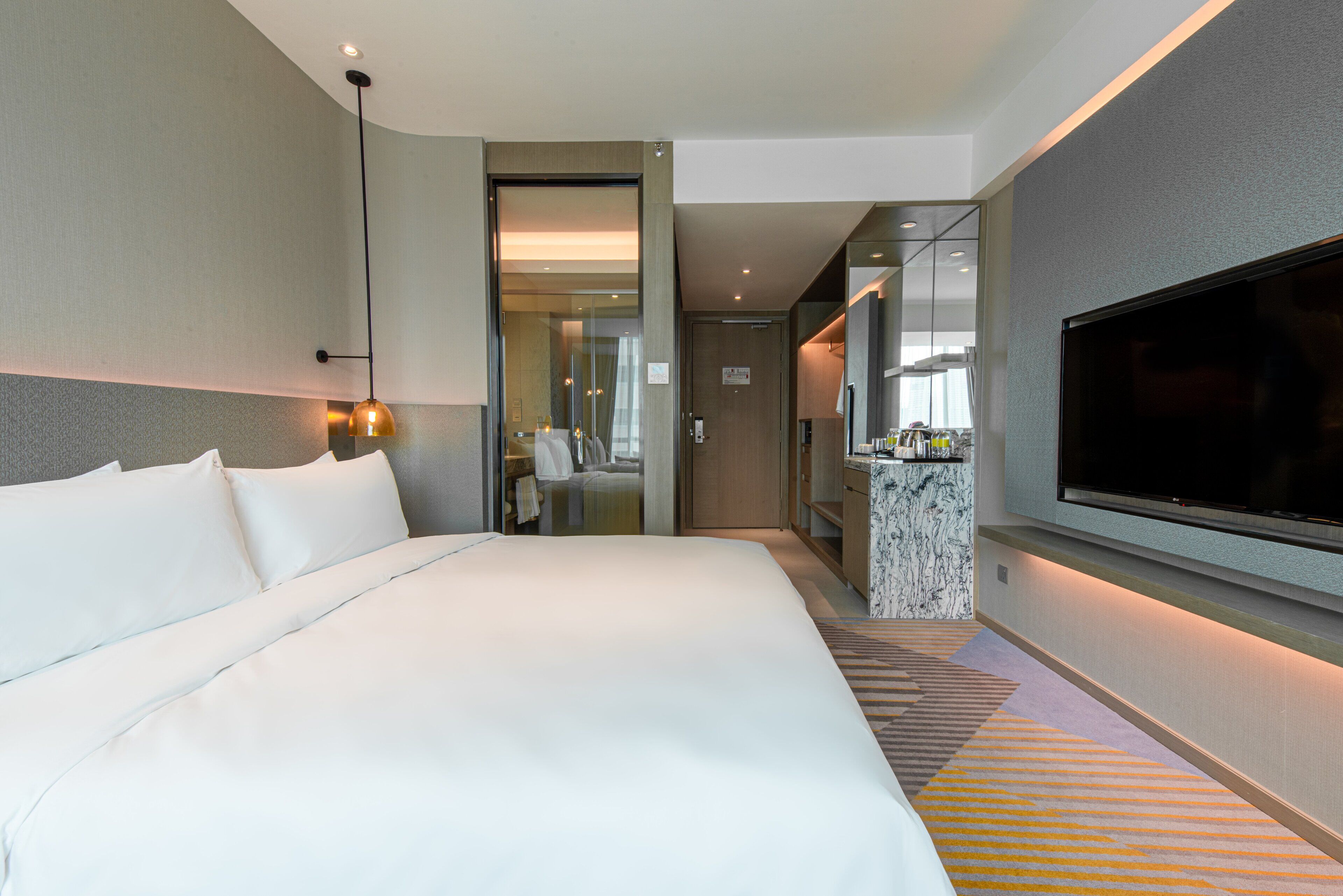 A modern hotel room with a large bed, a television, and a small kitchenette.