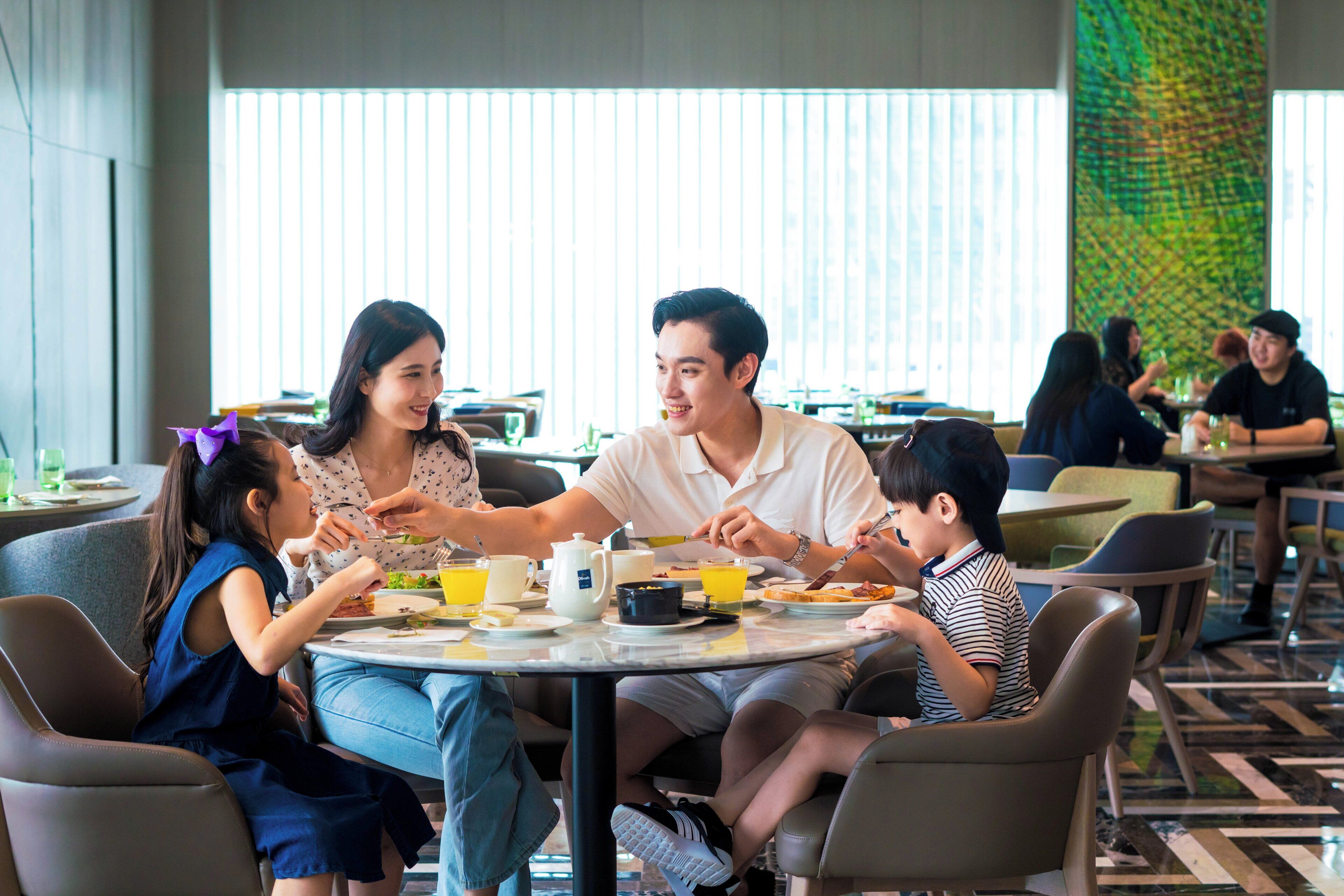 Un grupo de personas cenando en una mesa redonda en un restaurante moderno con ventanas amplias y un muro decorado.