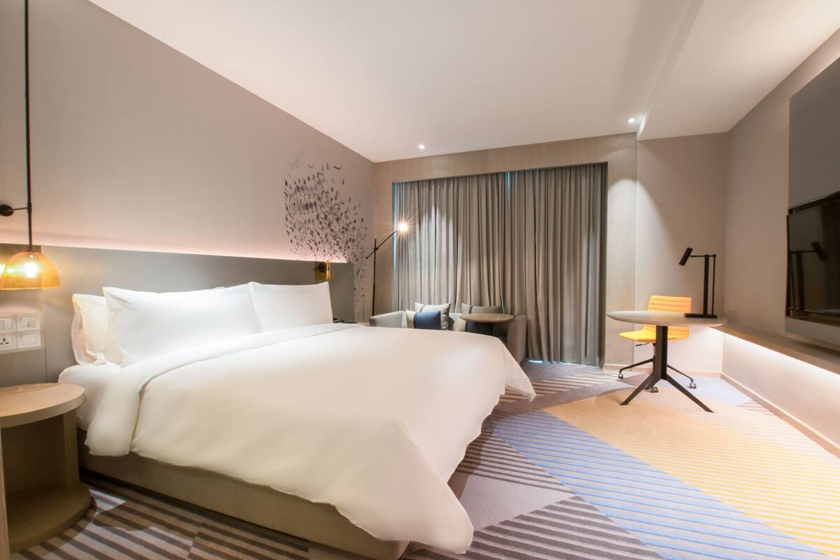 A modern hotel room with a large bed, a desk, a chair, and a TV.