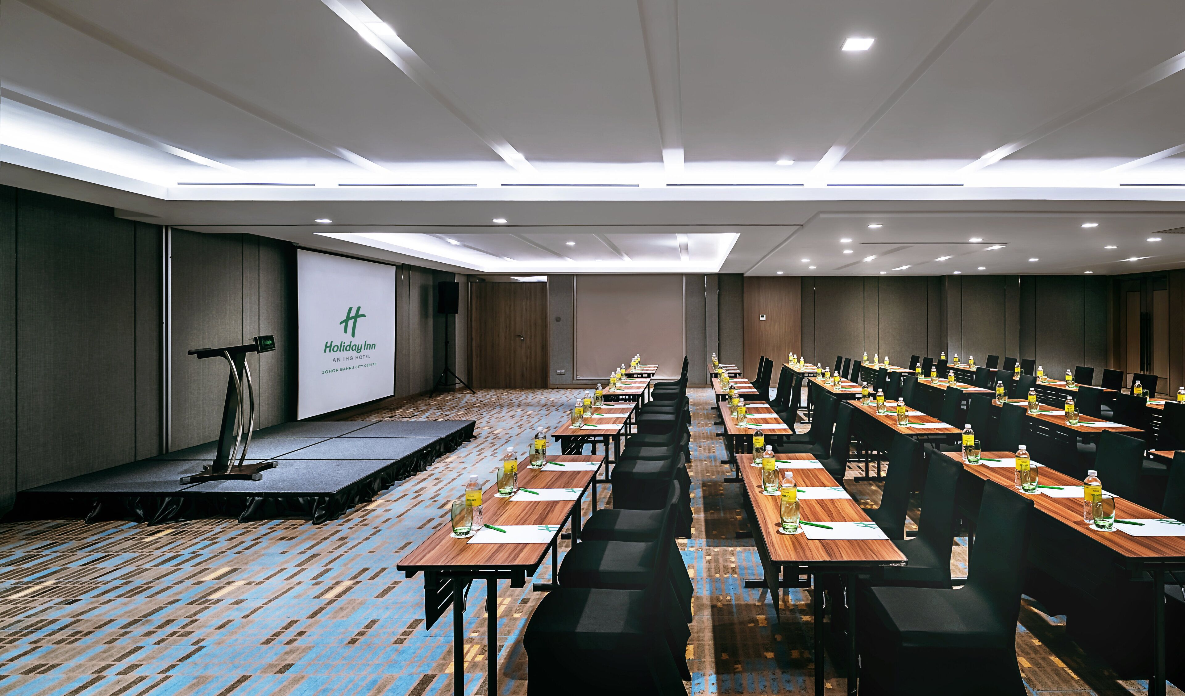 A conference room with a stage, multiple tables with chairs, and a projector screen.