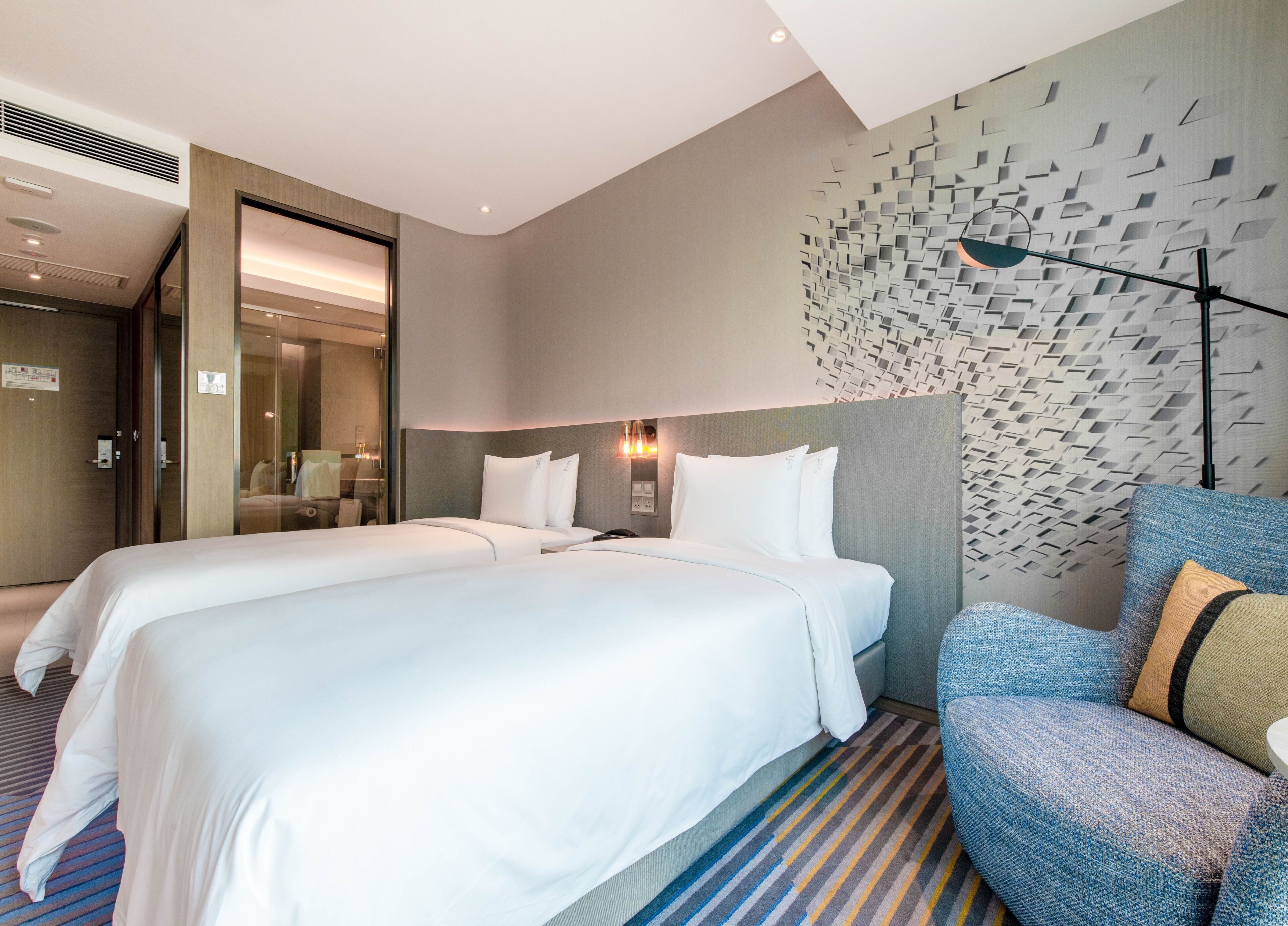 A hotel room with two beds, a seating area, and a decorative wall.