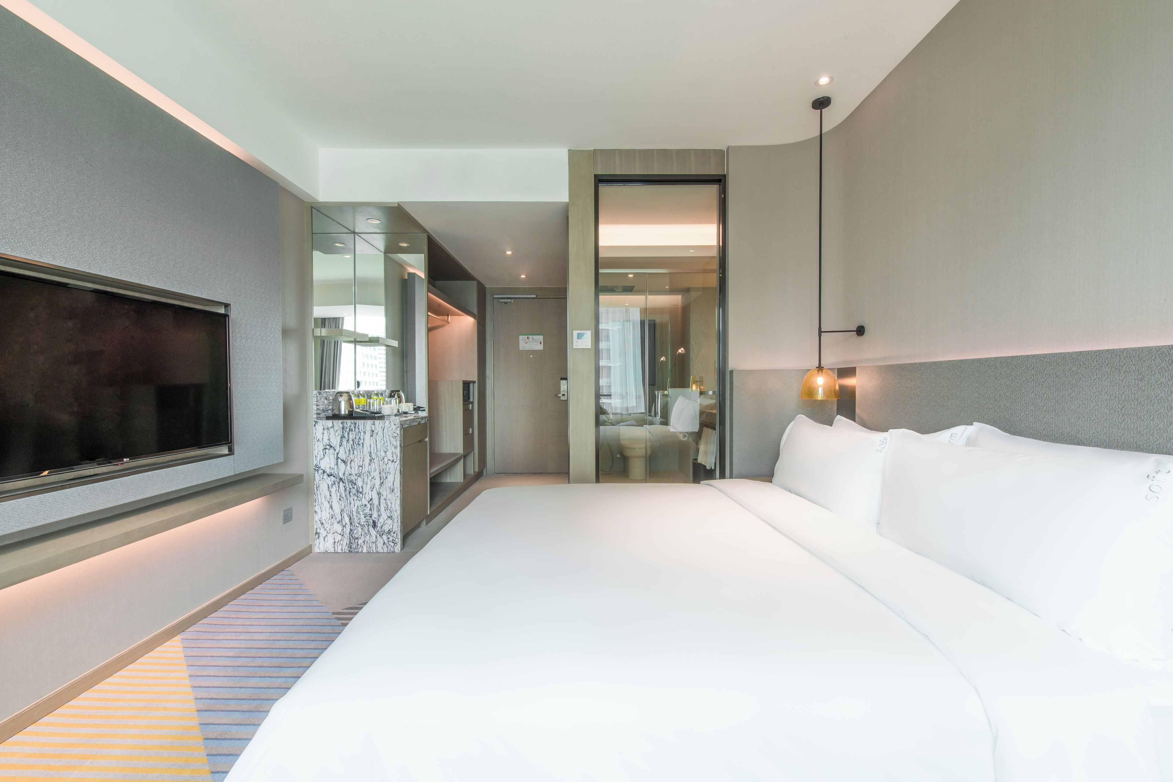 A hotel room with a large bed, a television, a minibar, and a bathroom visible through a glass door.