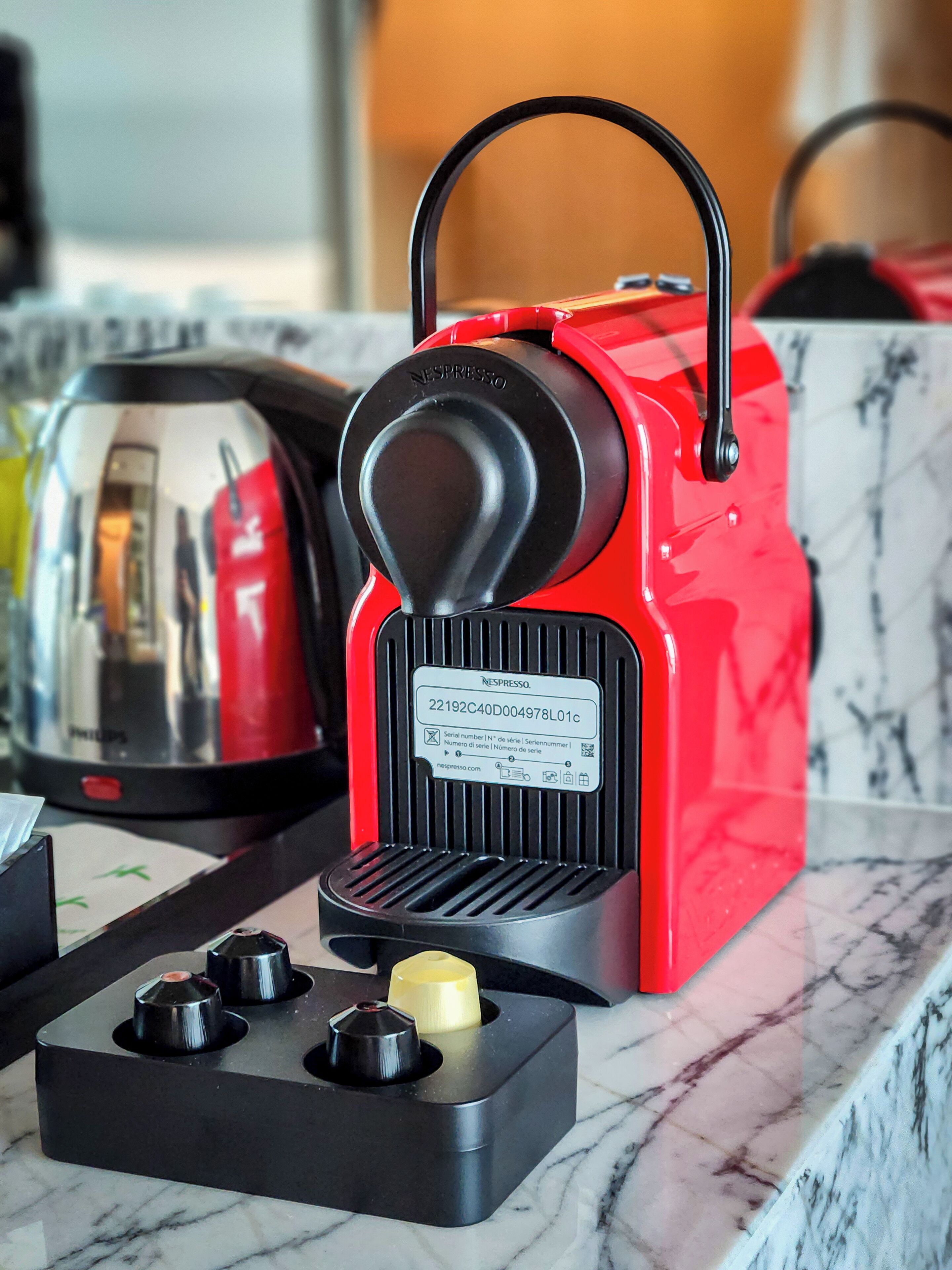 A red Nespresso coffee machine with a black base and a coffee pod dispenser on a marble countertop.