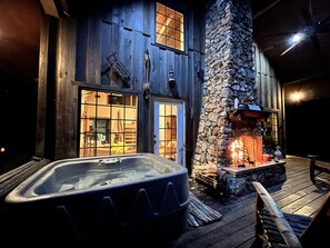 Un chalet rustique doté d’une cheminée en pierre, d’un bain à remous et d’une terrasse en bois.