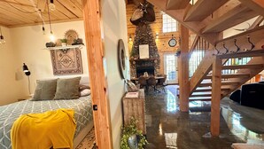 Um quarto aconchegante com uma cama, escadas de madeira, uma lareira de pedra e um espaço de jantar.