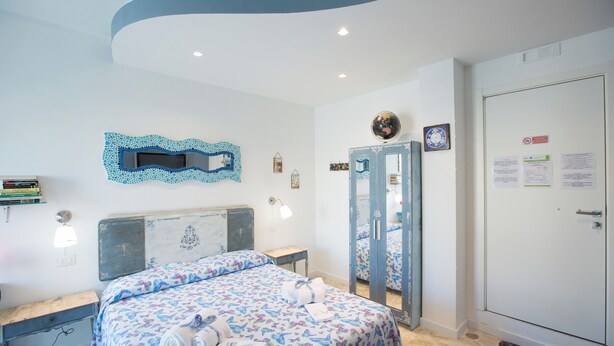 A hotel room with a bed, a desk, a mirror, and a wardrobe. - Room-versomare - Room Scirocco - Cis Ba (Polignano a Mare)