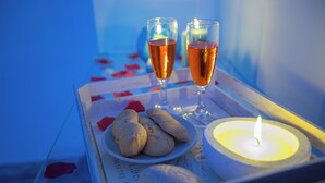 A tray with two glasses of amber liquid, a lit candle, and a plate of cookies on a table with a blue background. - Room-versomare - Room Scirocco - Cis Ba (Polignano a Mare)
