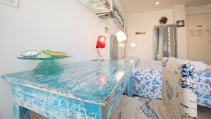 A room with a blue-painted table, a red lamp, and a bed with a patterned bedspread. - Room-versomare - Room Scirocco - Cis Ba (Polignano a Mare)