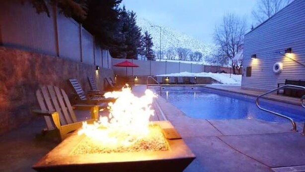 Zona de piscina con una chimenea, sillas de descanso y un área de estar cubierta.