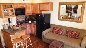 Cocina compacta con armarios de madera, un refrigerador negro y un comedor con mesa y sillas.