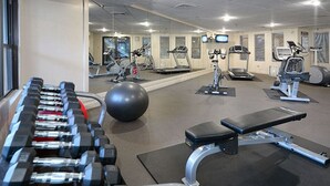 Un gimnasio con diverso equipamiento de ejercicio, incluyendo mancuernas, una pelota medicinal, cintas de correr y bicicletas estáticas.