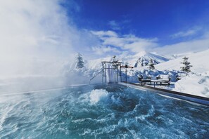 Un espace extérieur enneigé comprenant une piscine chauffée, des bancs et une structure métallique.
