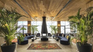 A spacious lobby with a wooden ceiling, large potted plants, a central seating area with sofas and a coffee table, and large windows offering a view. - Gudauri Lodge (GUDAURI)