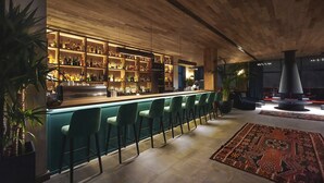 A bar area with a long counter, multiple shelves of bottles, and green bar stools. - Gudauri Lodge (GUDAURI)