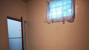 A bedroom with a bed, a window with lace curtains, a door, and a small table with a plant. - Apartment casa de mami, Turrialba (Turrialba)