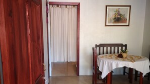 A room with a wooden door, a dining table with a white tablecloth, a chair, and a painting on the wall. - Apartment casa de mami, Turrialba (Turrialba)