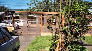 A parking area with a gated entrance, a parked car, and a small garden with a tree and shrubs. - Apartment casa de mami, Turrialba (Turrialba)