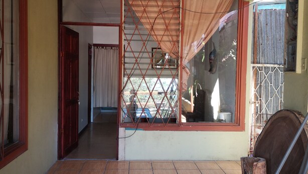 A room with a tiled floor, a sliding door with a mesh screen, a chair, and a window with a view of the outside. - Apartment casa de mami, Turrialba (Turrialba)