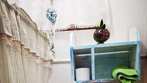 A bathroom with a striped curtain, a small sink, a toilet, a shelf with a toilet paper roll and a green towel, and a decorative item on the wall. - Apartment casa de mami, Turrialba (Turrialba)