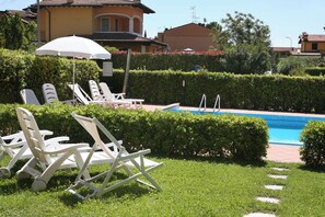 A pool area with lounge chairs and an umbrella, surrounded by well-maintained hedges and a clear blue pool.
