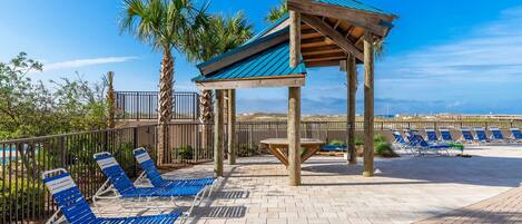 Un área de descanso en la playa con sillones azules y una estructura de pérgola de madera.